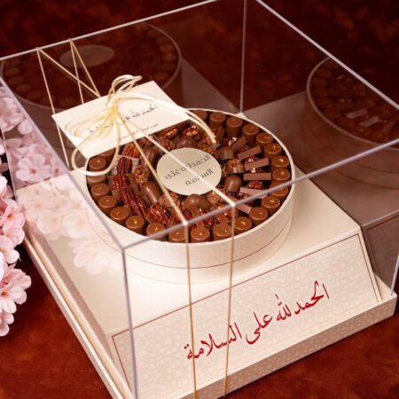 Luxury customized chocolate gift with milk chocolates and pecans in a round box inside a clear acrylic case with Arabic greeting