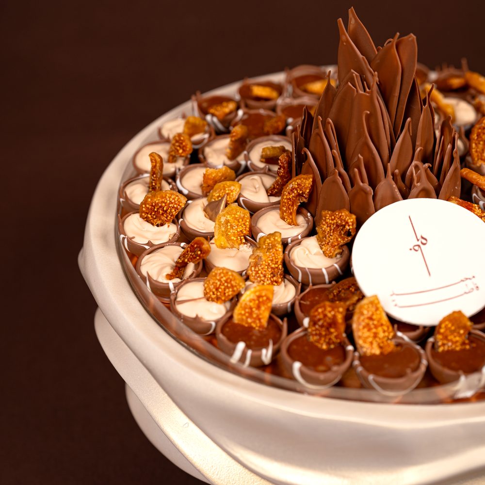 Luxury fig chocolate tray seen from above with cream-filled and chocolate-filled cups topped with dried fig around a chocolate flower