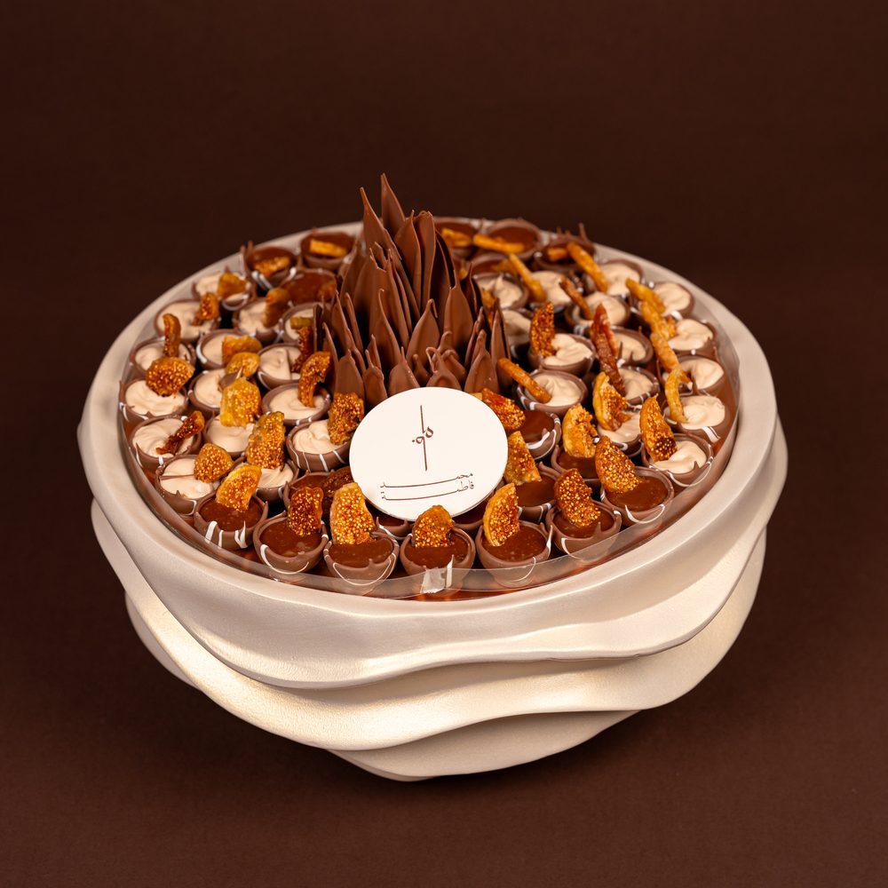 Luxury fig chocolate tray seen from above with cream-filled and chocolate-filled cups topped with dried fig around a chocolate flower