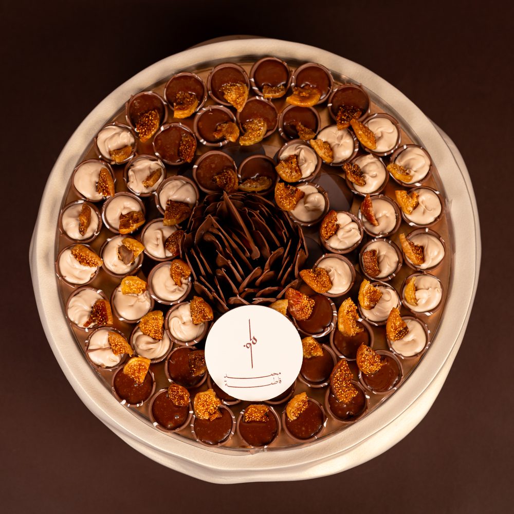 Luxury fig chocolate tray seen from above with cream-filled and chocolate-filled cups topped with dried fig around a chocolate flower