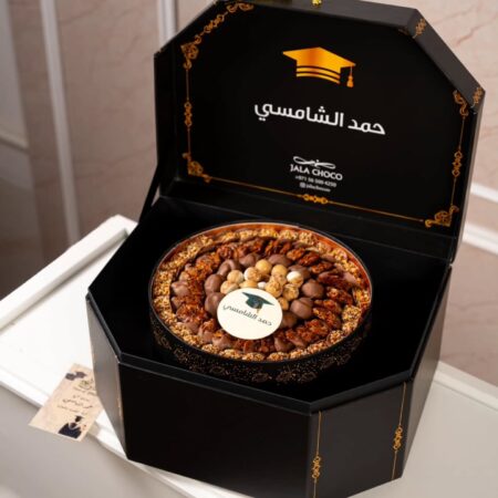 Open black octagonal graduation gift box with gold detailing and a round tray of arranged chocolates