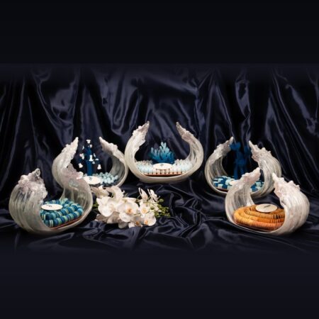 Five white wave centrepieces holding blue and caramel wedding chocolates with white orchids on navy satin