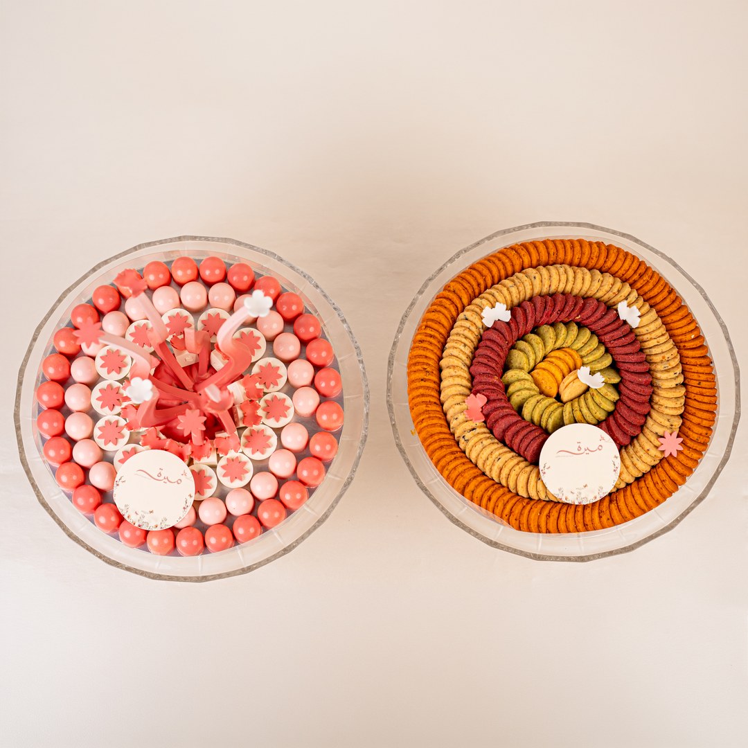 Top view of a pink chocolate tray beside a round tray of orange, red and green cookies