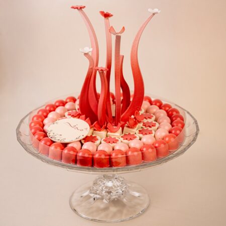 Round tray of red and pink dome chocolates under a clear lid on a crystal cake stand